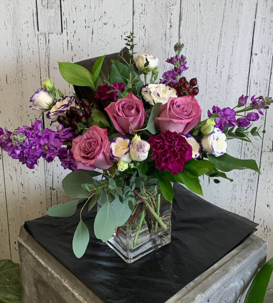 An image of a pink, purple and green flower arrangement in a glass vase
