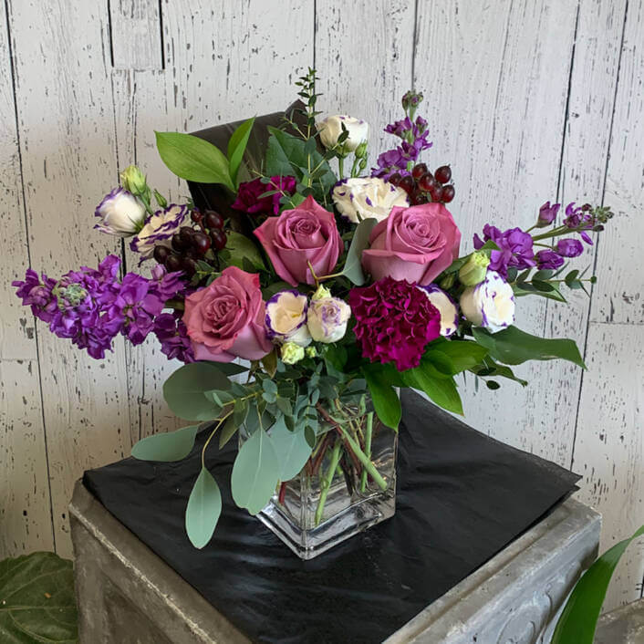 An image of a pink, purple and green flower arrangement in a glass vase