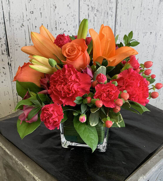 An image of a red and orange flower arrangement with lilly's, roses, and carnations
