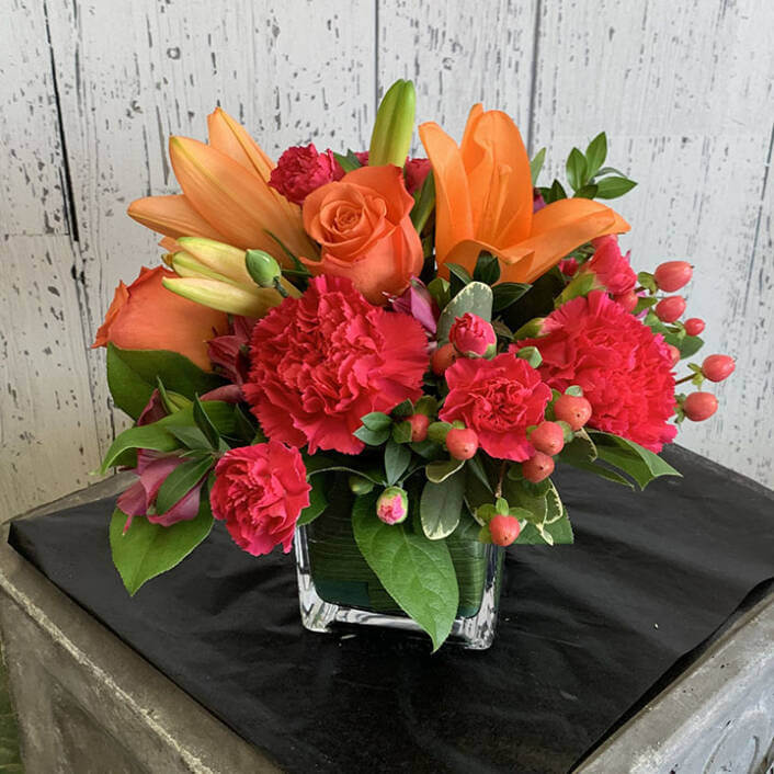 An image of a red and orange flower arrangement with lilly's, roses, and carnations