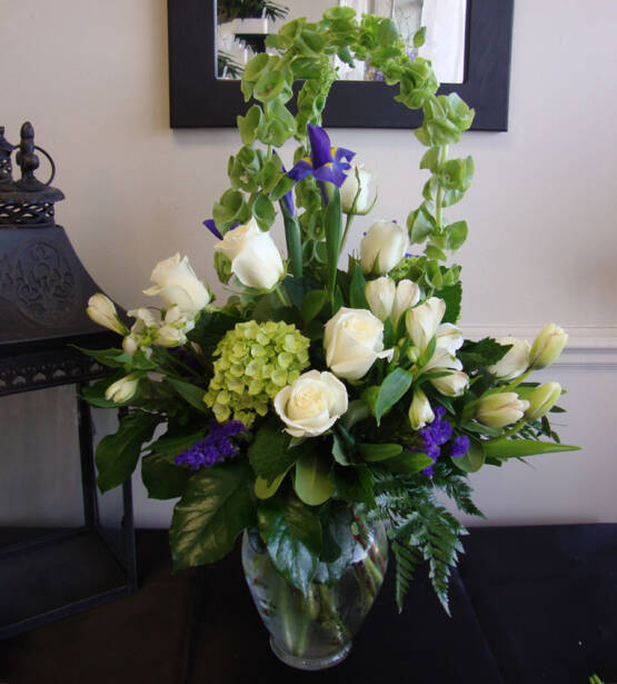 a purple white and green sypathy arrangement in a glass vase