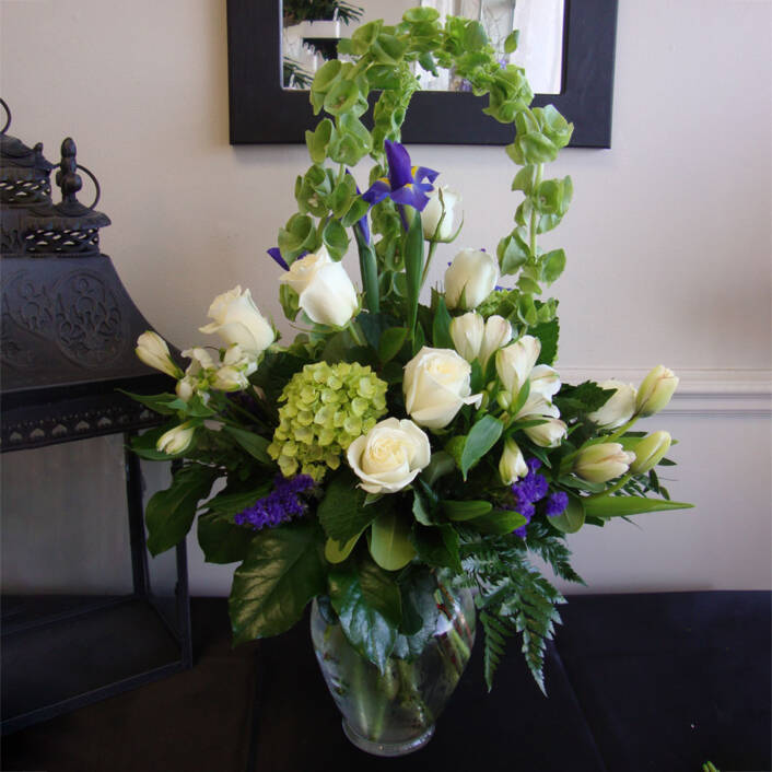 a purple white and green sypathy arrangement in a glass vase