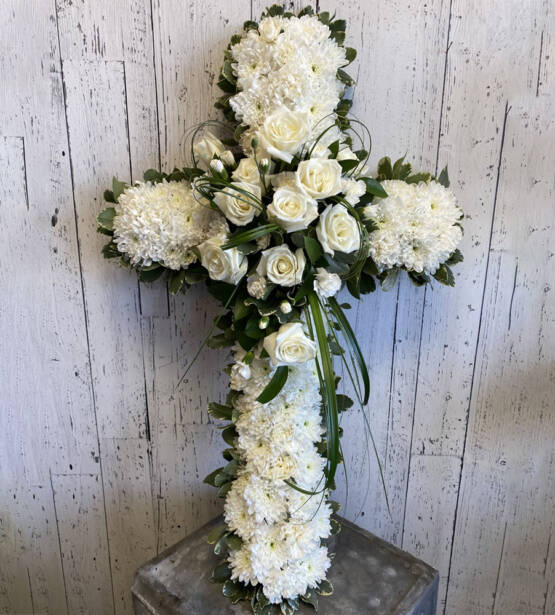 a cross shaped sympathy floral arrangement made with white roses and white carnations.