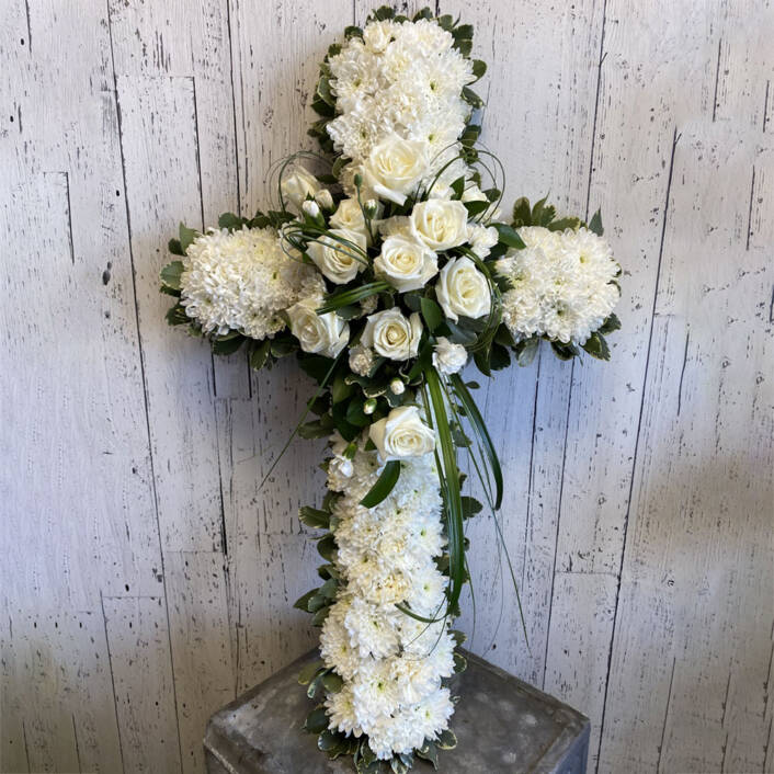 a cross shaped sympathy floral arrangement made with white roses and white carnations.