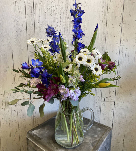 a lavender purple and green spring arrangement in a glass pitcher vase