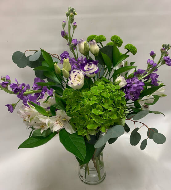 a purple green and white floral arrangement in a vase