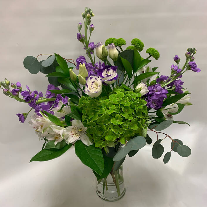 a purple green and white floral arrangement in a vase