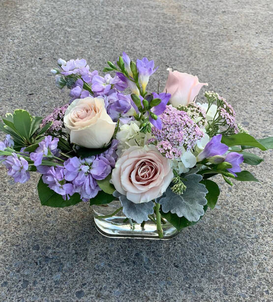 a purple and cream white floral arrangement in a glass square vase