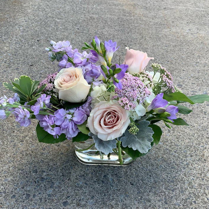 a purple and cream white floral arrangement in a glass square vase