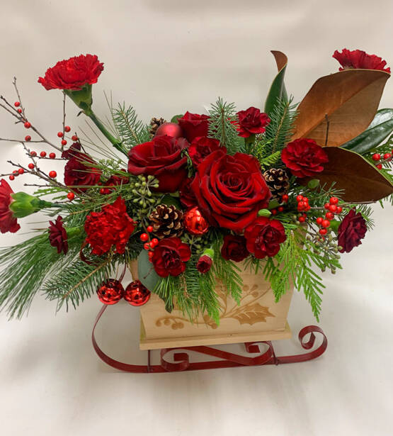 A red and green Christmas arrangement with pinecones in a wooden sleigh as an arrangement holder