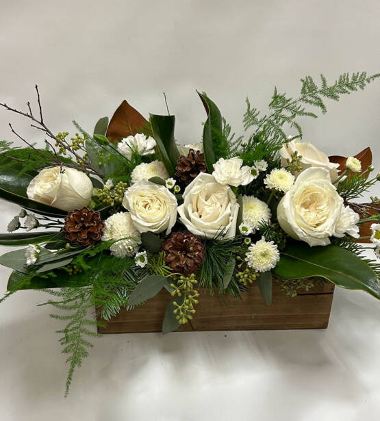 A white and green Christmas arrangement with pinecones in a wooden rectangular box.