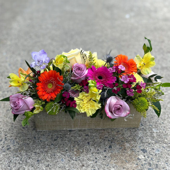 A colourful floral arrangement in a wooden rectangular box