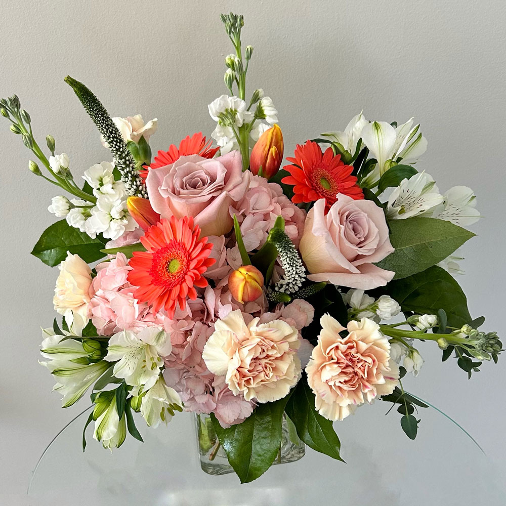 peachy-mama a peach spring floral arrangement in a square glass vase.
